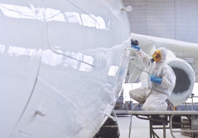 A person in white suit painting an airplane.